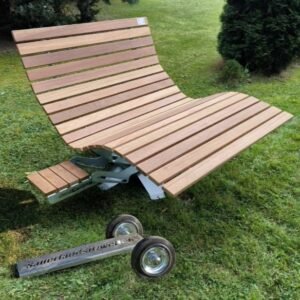 Ein geschwungenes Waldsofa aus Bangkirai-Holz mit integrierbarem, ausziehbarem Tisch. Davor liegt eine separate Transportvorrichtung mit zwei Rädern.